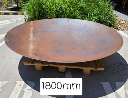 "Rustic Corten steel firepit with a circular design, showcasing natural weathering patina and unique texture. The firepit features a sturdy base and a deep bowl for safely containing flames and providing warmth. Surrounding the fire, people gather for cozy outdoor gatherings, enjoying the flickering glow and crackling sounds.